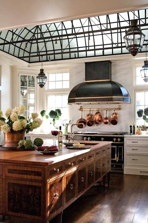 a refined vintage kitchen with shaker style cabinets, a black hood, a vintage table with plenty of storage, vintage metal lamps