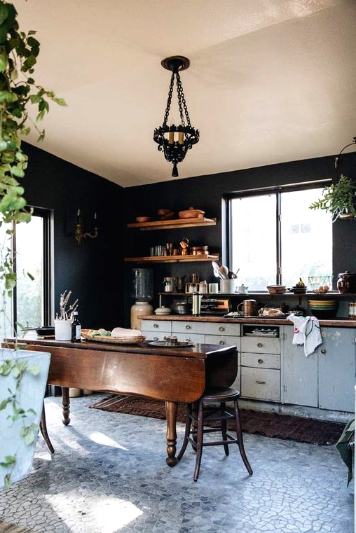 a stylish kitchen with black walls, white shabby chic cabinets, butcherblock countertops, a stained folding table as a kitchen island