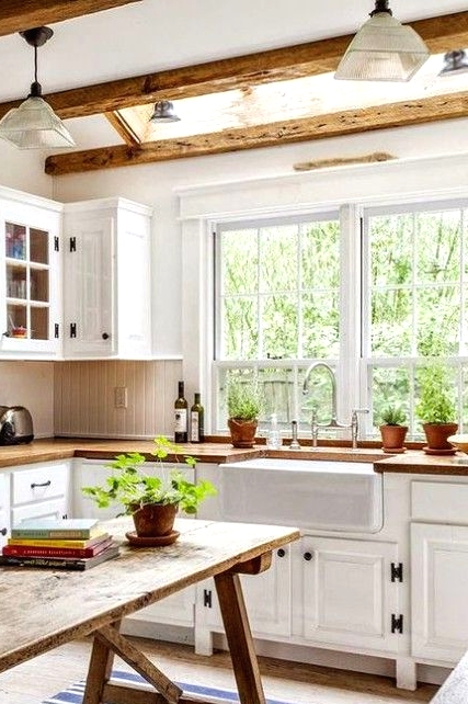 a welcoming farmhouse kitchen with white shaker cabinets, wooden beams on the ceiling, a wooden kitchen island that is a table
