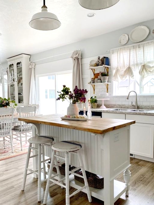 a white farmhouse kitchen filled with light, with a small wooden kitchen island with a stained countertop and tall white stools