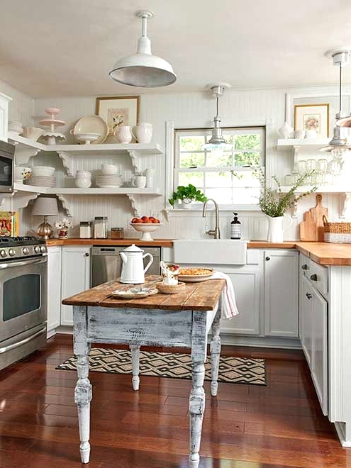 a white cottage kitchen with shaker style cabinets, butcherblock countertops, a shabby chic dining table that doubles as a kitchen island
