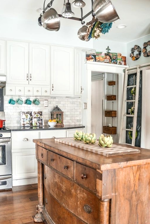 a white farmhouse kitchen with a marble tile backsplash, a vintage kitchen island that is a buffet, pretty artworks