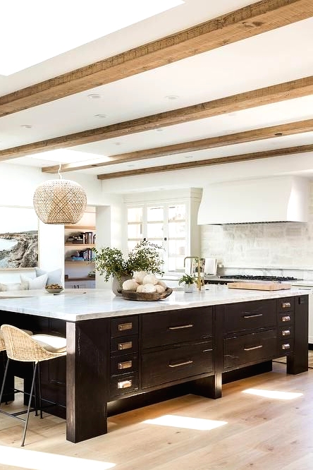 a white farmhouse kitchen with white stone countertops, wooden beams on the ceiling and a vintage black kitchen island with a white stone countertop