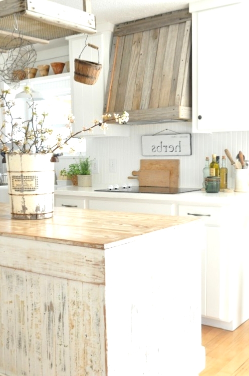 a white farmhouse kitchen with a shabby chic wooden kitchen island made of a cabinet, a reclaimed wooden hood and modern appliances and fixtures