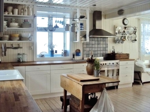 a white farmhouse kitchen with stained butcherblock countertops, stainless steel appliances and a folding stained dining table as a kitchen island