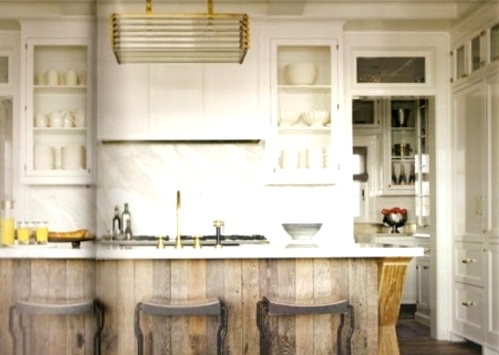 a white farmhouse kitchen with clear glass cabinets, a white marble backsplash and a reclaimed wood kitchen island with a marble countertop