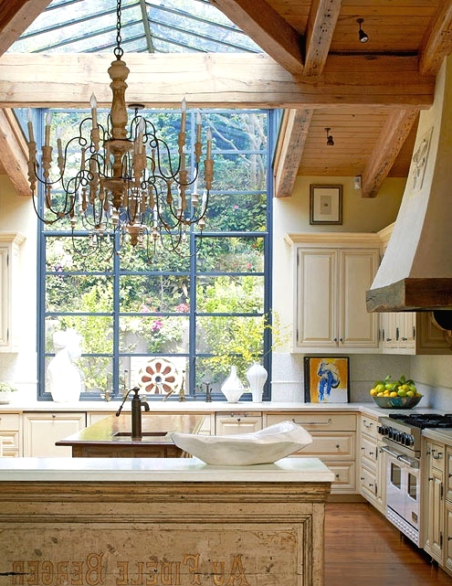 a large vintage kitchen in white and gold, with a large window and skylight, two vintage kitchen islands and a large vintage chandelier over it