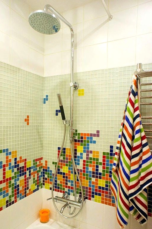 a bathroom with large scale white tiles and small scale green ones, with a bold and colorful tile mosaic and printed towels