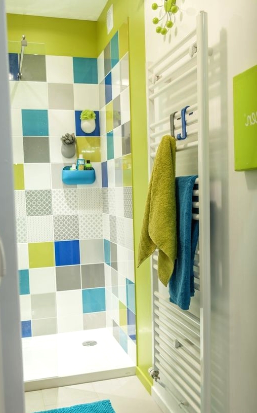 a bright bathroom in white accented with a neon green shower and multi-color tiles, with neon green and blue textiles