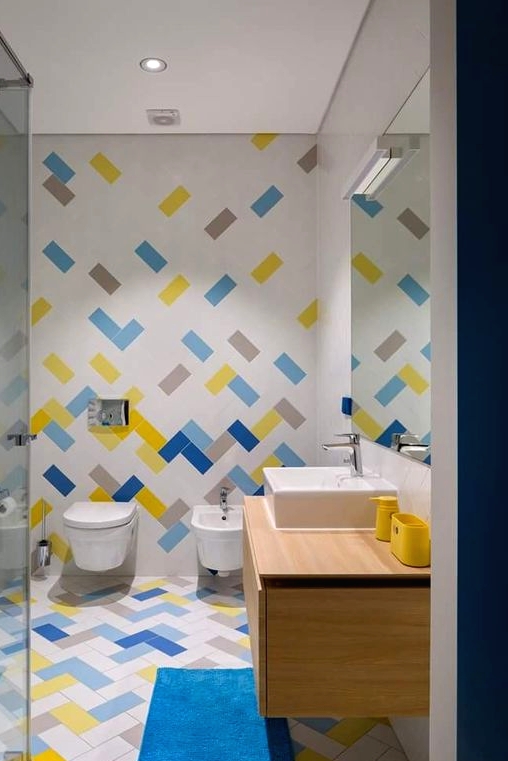 a contemporary white bathroom accented with bold light blue, electric blue, yellow and grey tiles, with a matching rug and a floating vanity