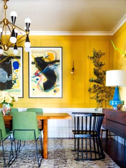 a colorful dining room with bold yellow walls, a stained table and credenza, green chairs and an elegant chandelier