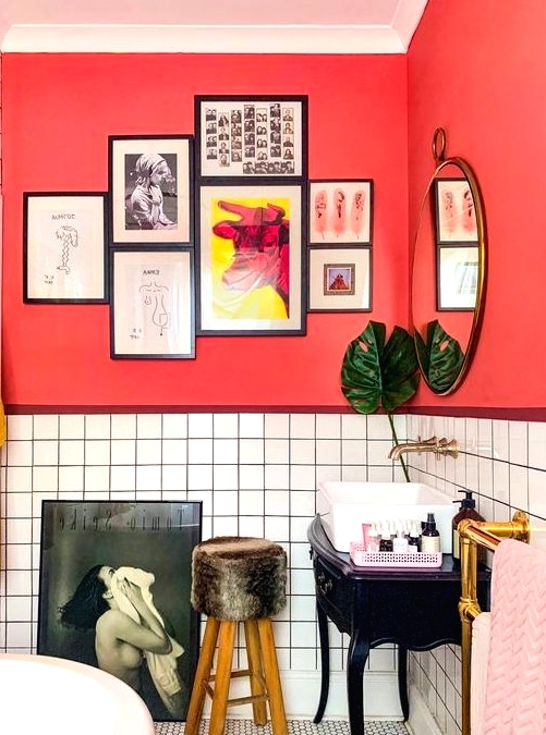 a unique bathroom with red walls, white tiles, pink and mustard textiles and quirky furniture and artworks