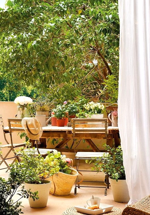 a beautiful Mediterranean terrace with a simple wooden dining table, potted plants and blooms, a jute pouf is very welcoming