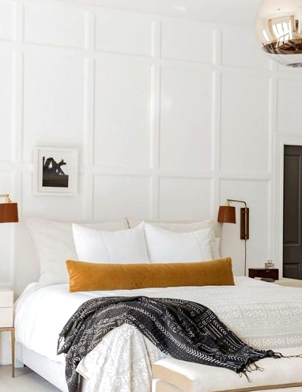 a sophisticated neutral bedroom with a creamy upholstered bed, an upholstered bench, leather sconces, white refined nightstands and paneled walls