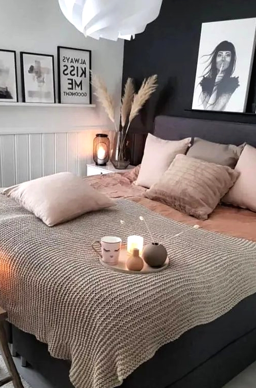 a stylish bedroom with a black accent wall, white paneling, a black bed with blush bedding and pretty artworks is very elegant