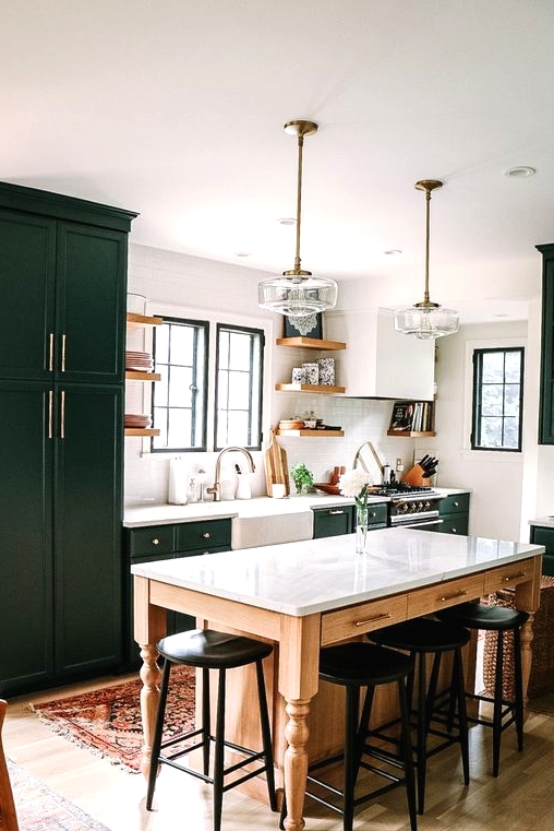 a dark green farmhouse kitchen with shaker style cabinets, a table that doubles as a kitchen island and black vintage stools