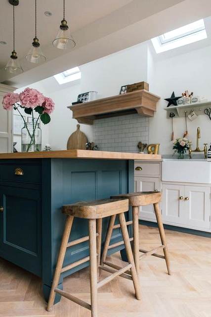 a farmhouse kitchen with creamy shaker style cabinets, a teal kitchen island with butcherblock countertops, wooden stools and a delicate hood