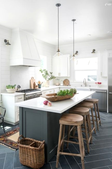 a farmhouse kitchen with white cabinets and a large hood, pendant lamps, a graphite grey kitchen island and wooden stools