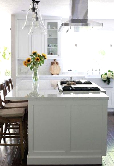 a lovely modern white kitchen with shaker cabints, stained chairs, glass pendant lamps and a white marble tile backsplash