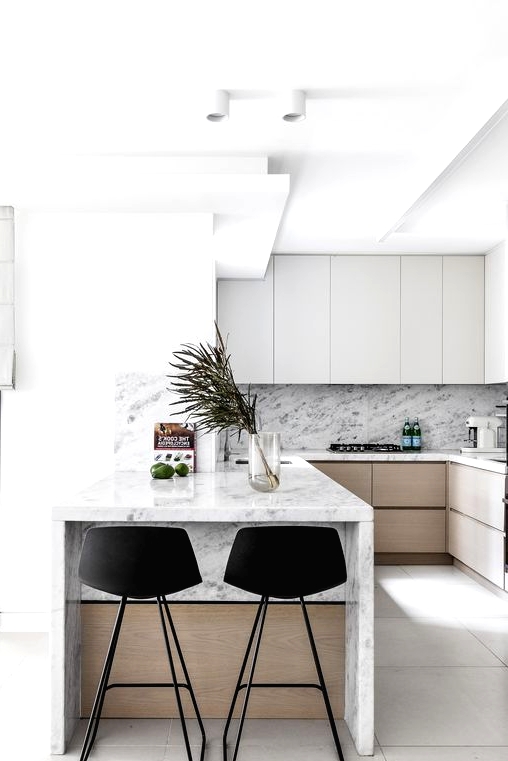 a minimalist kitchen with sleek grey and stained cabinets, a white marble backsplash and countertops, a small kitchen island with black stools