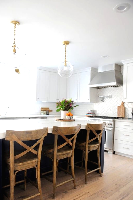 a modern kitchen with white shaker style cabinets, a navy kitchen island with stained stools and pendant lamps on chain