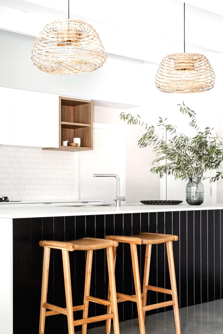 a refined contrasting kitchen with sleek white cabinets, a white subway tile backsplash, a large kitchen island with black planks, woven pendant lamps