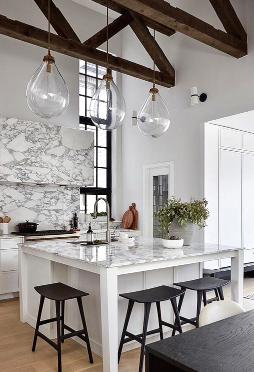a sophisticated white kitchen with marble touches, a small kitchen island with a seating zone and black stools here