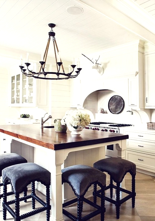 a white farmhouse kitchen with shaker style cabinets, a small kitchen island with a seating space and black stools plus a black vintage chandelier