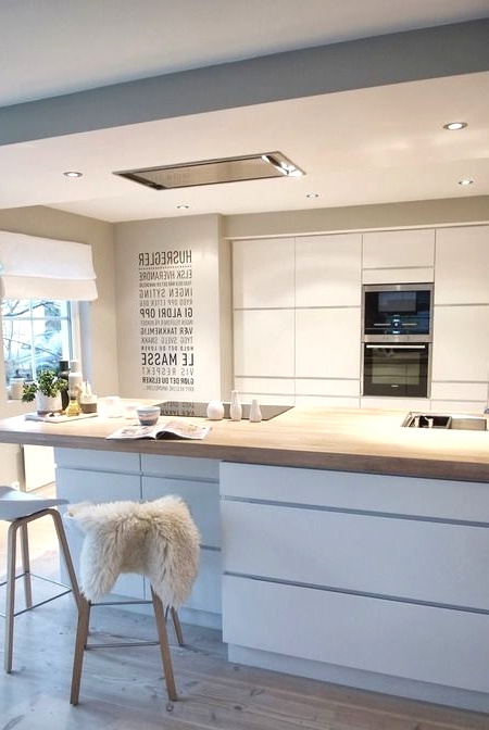 a minimalist Scandinavian kitchen with sleek white cabinets, built-in lights, a large kitchen island with a small seating space and tall stools