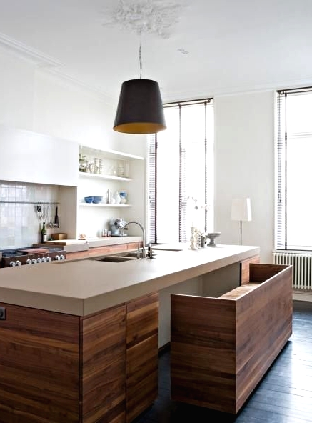a chic minimalist kitchen with stained and white sleek cabinets, tan stone countertops, a bench that integrates seasmlessly into the kitchen island and a pendant lamp