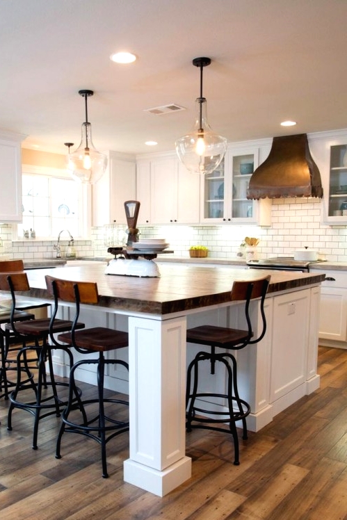 a white farmhouse kitchen with shaker style cabinets, butcherblock countertops, a large kitchen island with a seating space and vintage tall stools