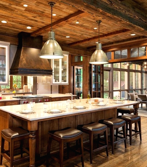 a beautiful chalet kitchen with wooden cabinets, walls, ceiling and beams, a large kitchen island in vintage style and dark leather stools for eating here