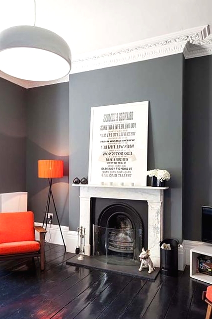 a catchy modern living room with slate grey walls, a fireplace, bold orange pieces - lamps, chairs is a chic and contrasting space