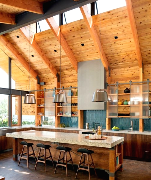 a contemporary barn kitchen with skylights, wooden beams, stained cabinets and a kitchen island, cabinets with sliding doors and metal lamps