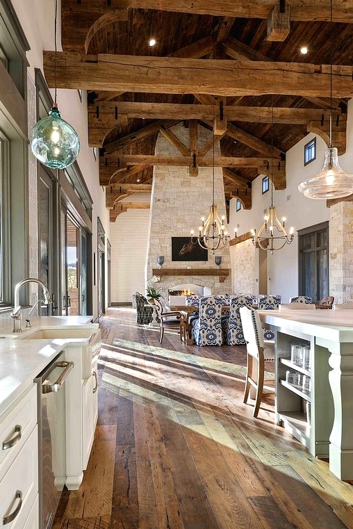 a neutral barn space with white kitchen cabinets, stained wooden beams, pendant lamps and chandeliers