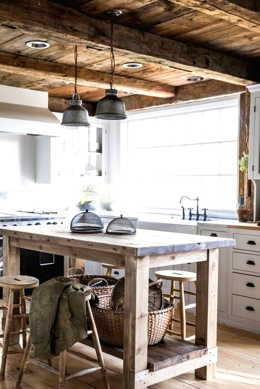 a rustic barn kitchen with white planked cabinets, a relcaimed wood kitchen island and stools, a weathered and aged wood ceiling with beams