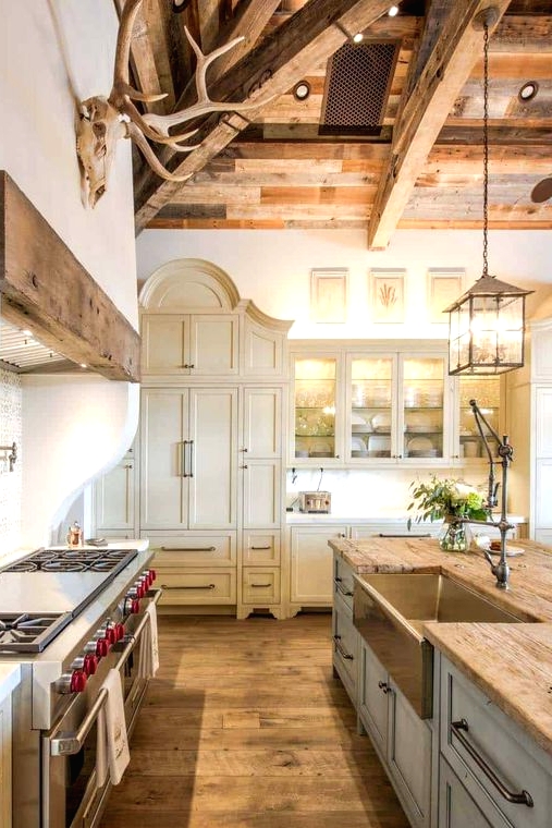a refined vintage barn kitchen with a wooden ceiling with beams, creamy shaker style cabinets, a light blue kitchen island, butcherblock countertops and pendant lamps