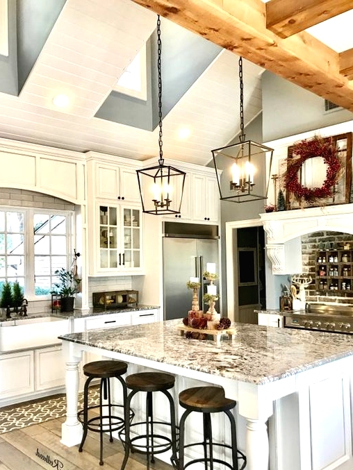 a white barn kitchen with skylights and wooden beams, white shaker cabinets and a large kitchen island, vintage black pendant lamps