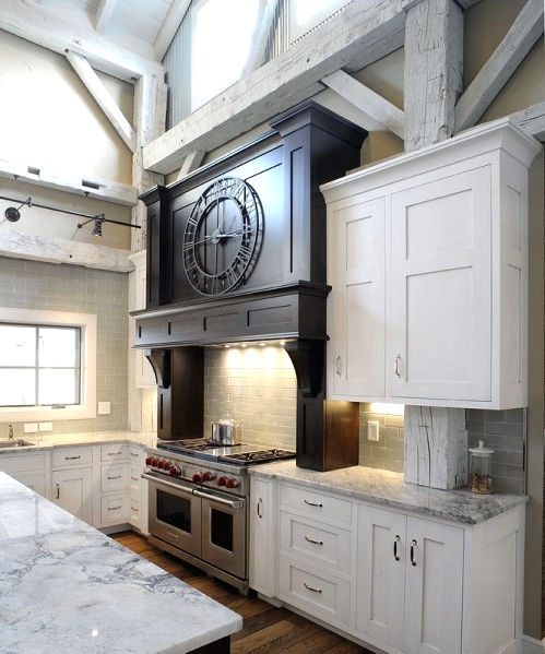 a white barn kitchen with white shaker style cabinets, white stone countertops, a black kitchen island for a contrast and whitewashed wooden beams for a cozy feel