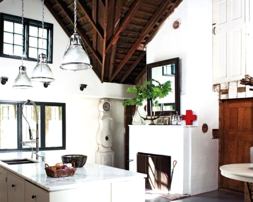 a modern white barn kitchen with a cool kitchen island and glass pendant lamps, a fireplace with a cool screen, a dark wooden ceiling with beams