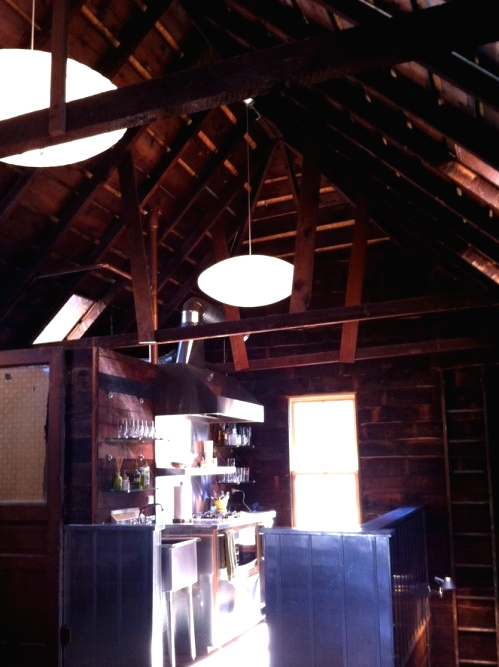 a dark barn kitchen fully clad with dark-stained wood, with wooden and metal cabinets, pendant lamps and not much natural light