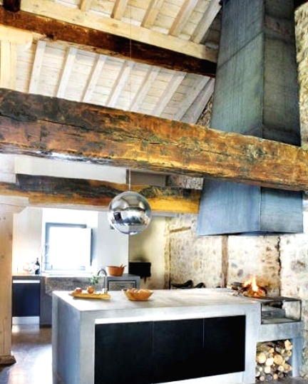 a barn kitchen with a whitewashed ceiling, wooden beams, concrete cabinets, a large hood covered with metal sheets is a cozy wabi-sabi space