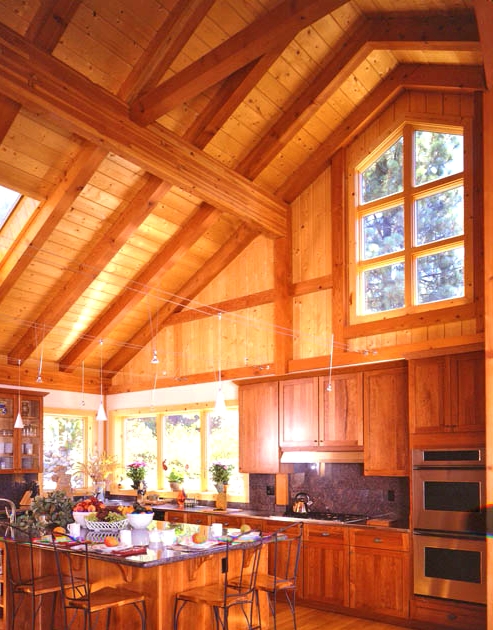a light-stained wood clad kitchen with windows and skylights, with stained shaker-style cabinets, a wooden kitchen island and black metal stools