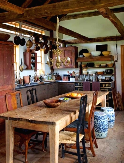 a vintage barn kitchen with wooden beams, vintage shabby chic cabinets, pans hanging on the beams and a wooden dining set
