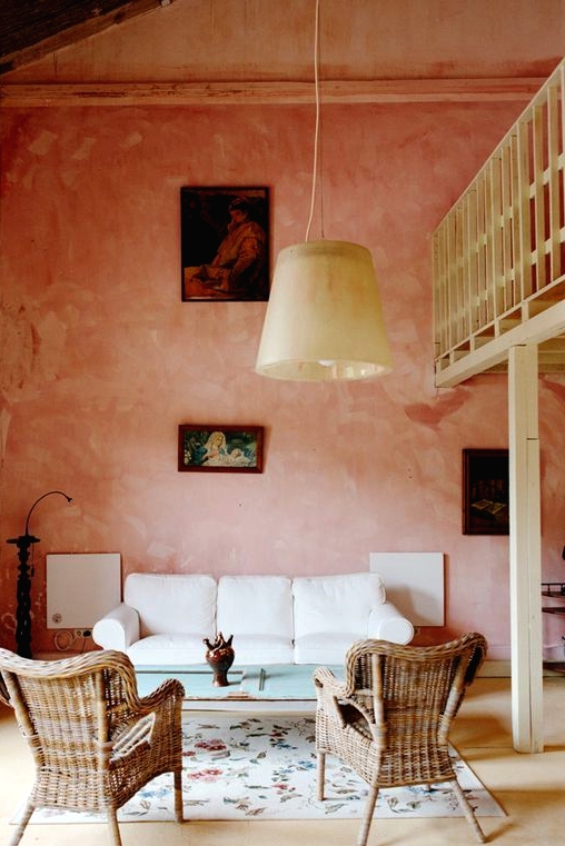a beautiful living room with pink limewashed walls, a white sofa, woven chairs, a delicate table and a pendant lamp