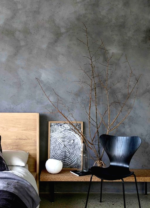a catchy bedroom with grey limewashed walls, light-stained furniture and a black plywood chair, branches in a vase
