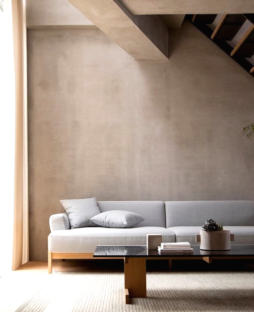 a contemporary Japandi living room with greige limewashed walls, a grey sofa and a glass coffee table plus a textural rug
