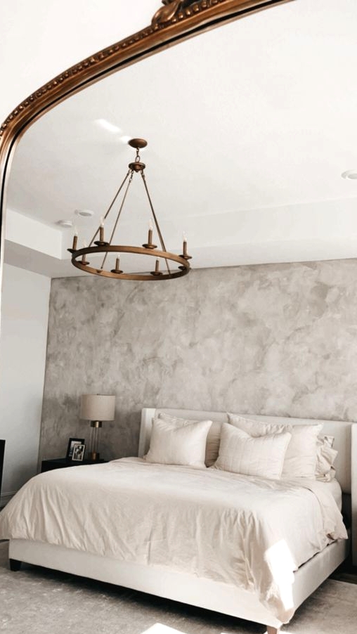 a delicate bedroom with grey limewashed walls, a creamy bed with matching bedding, black nightstands and neutral table lamps