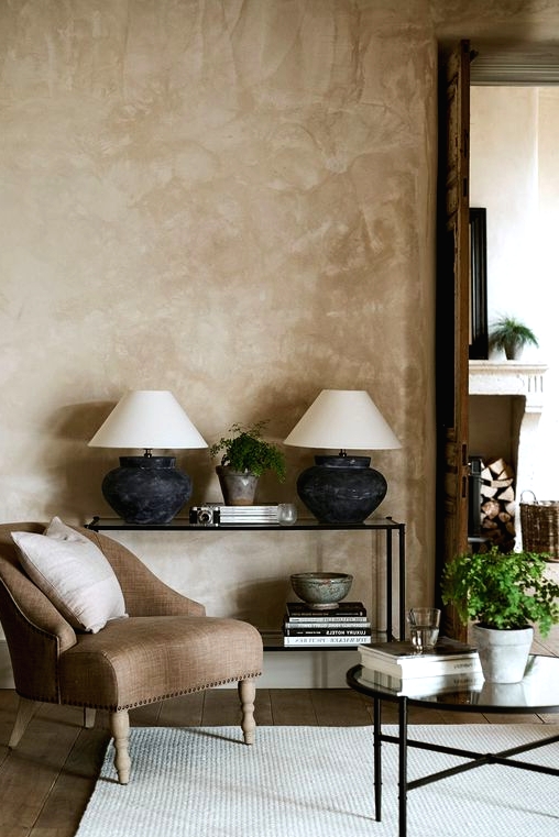 an elegant living room with beige limewashed walls, a glass console and coffee table, a brown chair and neutral textiles