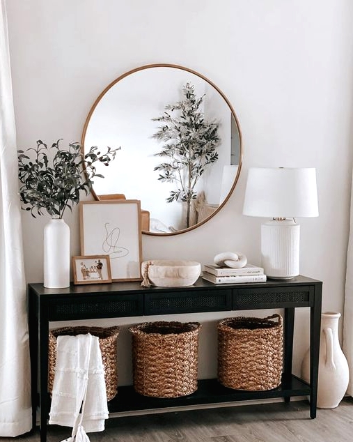 a black wooden console table, three baskets for storage, books, art and a bowl, a white table lamp and greenery branches in a vase